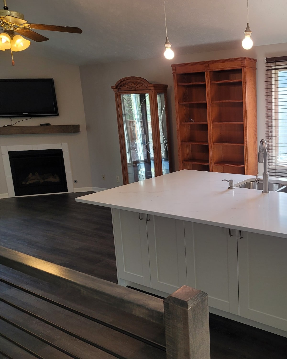 After, the same great room remodeled by Hansen Construction with LVP flooring, a waterfall-quartz island and a new wood mantel