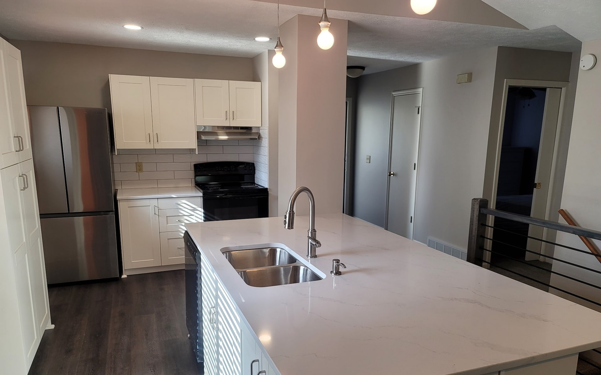 A finished kitchen remodel by Hansen Construction with white cabinets and a waterfall quartz island in Bellevue, NE